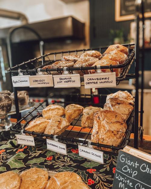 A display of baked goods including muffins and scones, labeled with their flavors, on a decorative tablecloth.