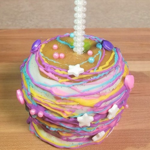 Colorful layered cake with swirls of icing, decorated with beads and stars, topped with a pearl-like candle.