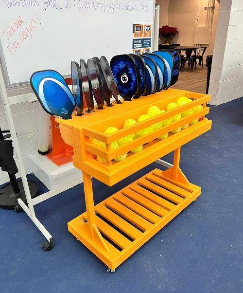 A bright orange rack holding various sports equipment, including discs and balls, in a gym or recreational space.