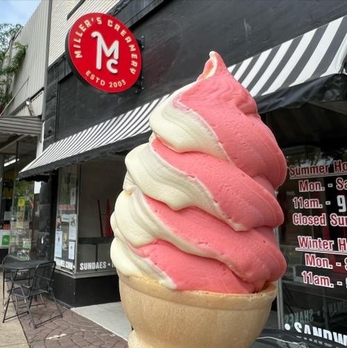 A large swirl of pink and white soft serve ice cream in a cone, in front of Miller's Creamery shop.