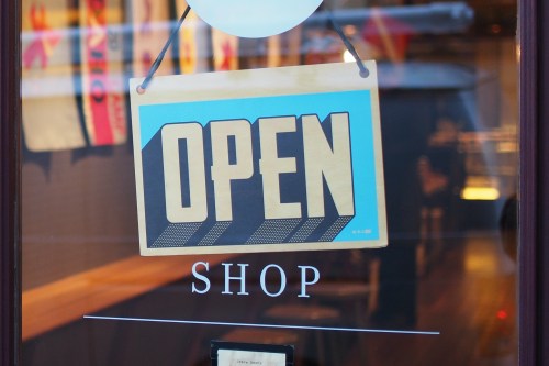 A colorful "OPEN" sign hanging in a shop window, with the word "SHOP" displayed below it.