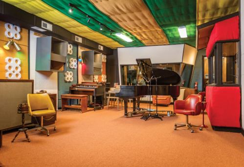 A music studio featuring a grand piano, vintage instruments, and colorful acoustic panels on the ceiling.