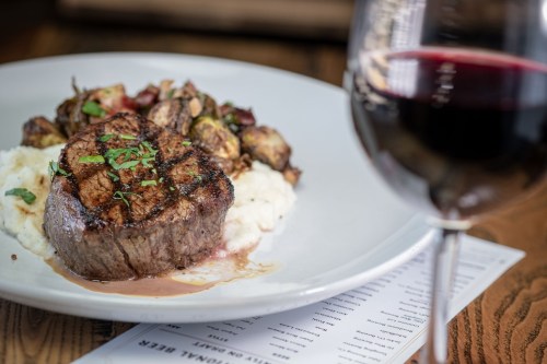 A perfectly cooked steak on a plate with mashed potatoes and roasted vegetables, accompanied by a glass of red wine.