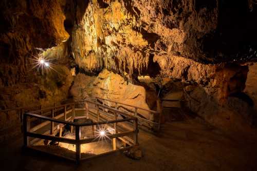 A dimly lit cave interior with rock formations and wooden railings, illuminated by soft lights.