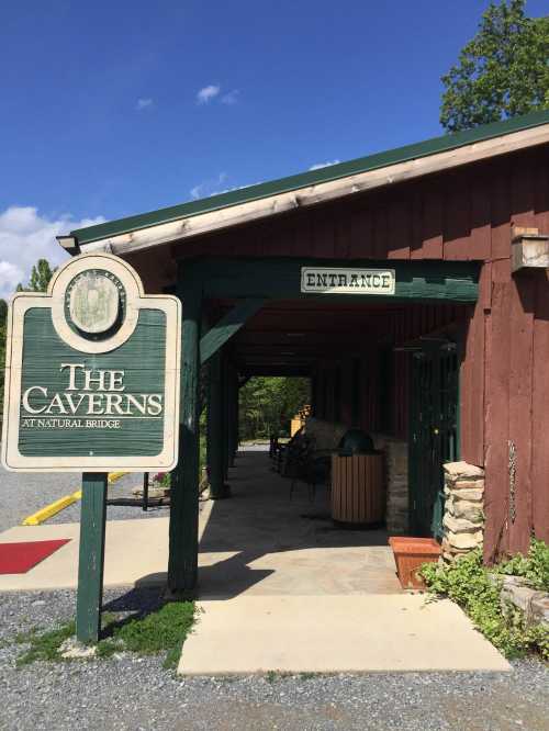 Entrance to The Caverns at Natural Bridge, featuring a wooden building and a sign. Clear blue sky above.