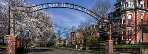 Archway sign reading "Willa-Ann Historic District" with blooming trees and historic buildings in the background.