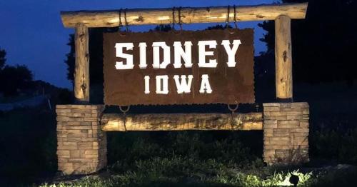 Sign for Sidney, Iowa, illuminated at night, featuring wooden and stone elements.