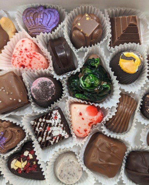 A variety of colorful chocolates arranged in a box, featuring different shapes and designs, including hearts and crowns.