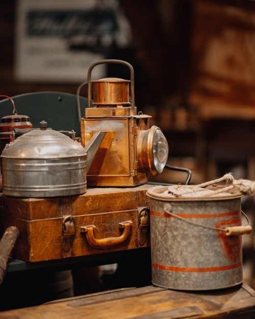A collection of vintage metal items, including a lantern, kettle, and bucket, arranged on a wooden surface.