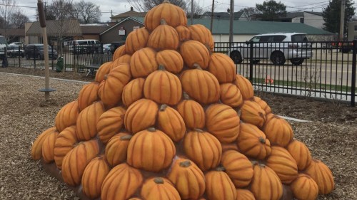 A large pyramid made of stacked orange pumpkins in a park setting.