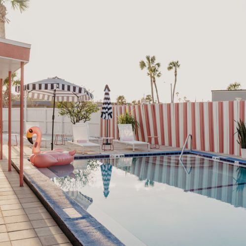 A serene pool scene featuring a pink flamingo float, lounge chairs, and striped umbrellas under a clear sky.