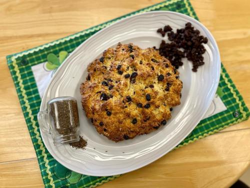 A freshly baked loaf of soda bread with raisins, served on a white platter alongside a jar of spices.