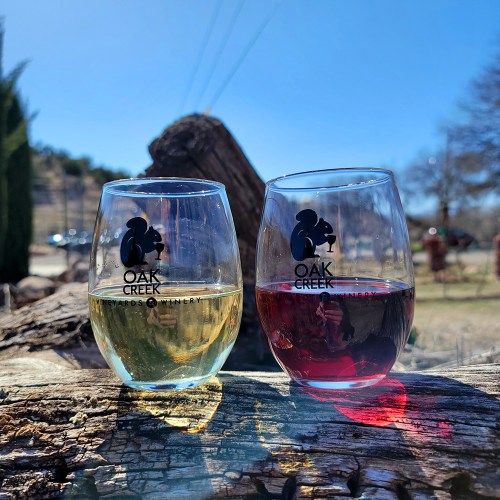 Two wine glasses, one with white wine and the other with red, sit on a log against a clear blue sky.