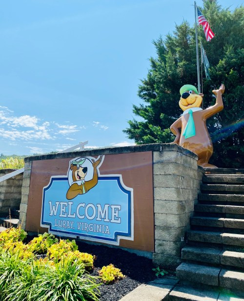Welcome sign for Luray, Virginia, featuring a cartoon character and surrounded by greenery and a clear blue sky.