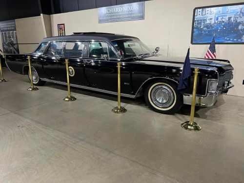 A vintage black limousine with presidential flags, displayed in a museum setting, associated with Richard Nixon.