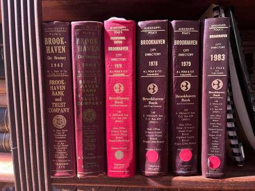 A collection of vintage city directories for Brookhaven, Mississippi, spanning from 1962 to 1983, on a wooden shelf.
