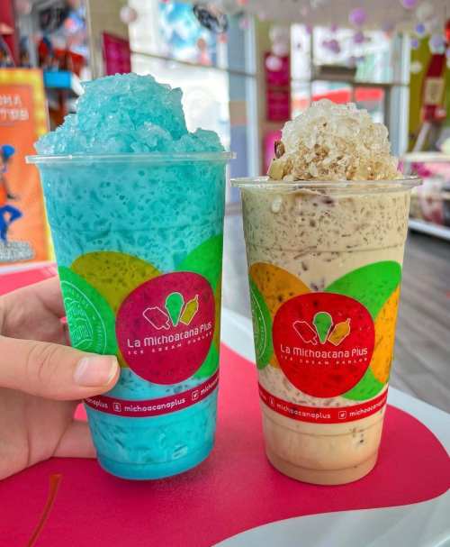 Two colorful drinks in clear cups: one blue and one beige, both topped with ice, held against a vibrant background.