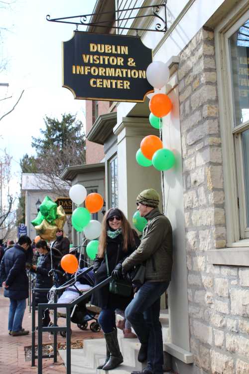 A couple stands outside the Dublin Visitor & Information Center, surrounded by festive balloons in green, white, and orange.