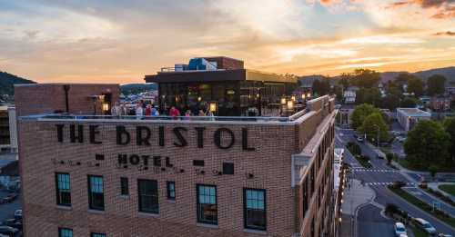 Aerial view of The Bristol Hotel at sunset, with people on the rooftop and a scenic landscape in the background.