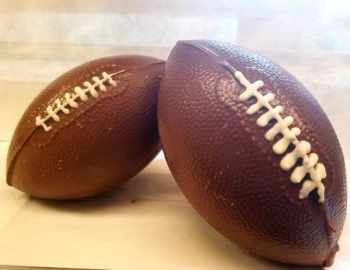Two chocolate footballs with textured surfaces and white laces, placed on a light background.