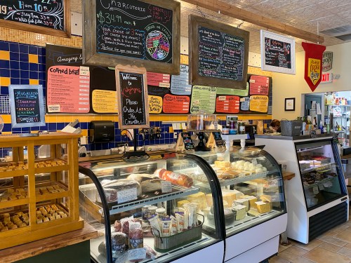 A cozy deli display with various cheeses, meats, and colorful chalkboard menus on the walls.