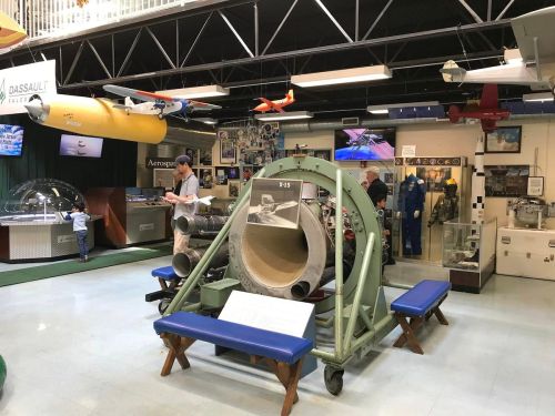 A museum exhibit featuring aircraft models, historical displays, and a large circular apparatus in the foreground.