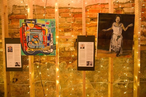 Two artworks displayed on wooden panels with string lights, featuring colorful abstract art and a portrait of a woman.