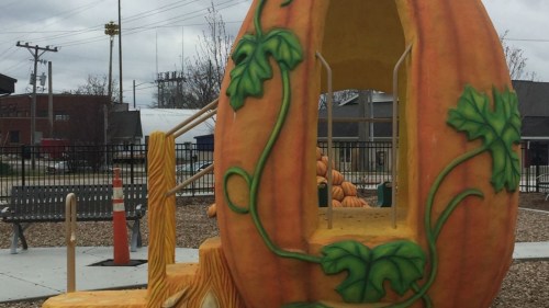 A large pumpkin-shaped play structure with green vines, set in a playground with a cloudy sky in the background.
