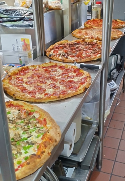 A variety of pizzas on a counter, including pepperoni, meat, and veggie options, in a kitchen setting.