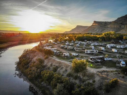 Aerial view of an RV park by a river at sunset, surrounded by hills and trees.