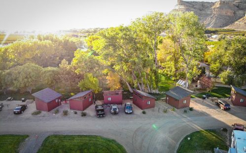 Aerial view of red cabins lined along a gravel path, surrounded by trees and a scenic landscape.