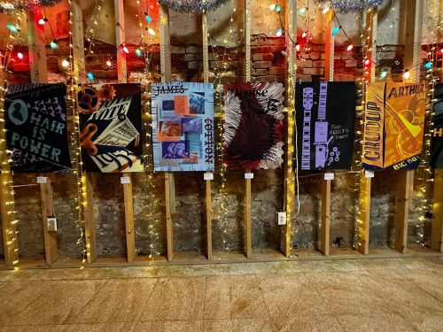 A wall display of colorful art pieces illuminated by string lights in a rustic setting.