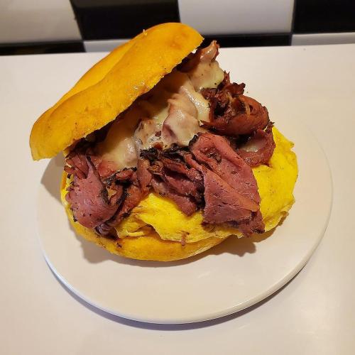 A hearty sandwich with layers of roast beef and melted cheese on a yellow bun, served on a white plate.