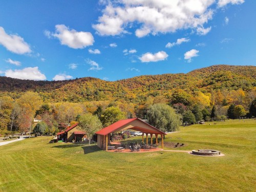 A scenic view of a grassy area with pavilions, surrounded by colorful autumn trees and blue skies.