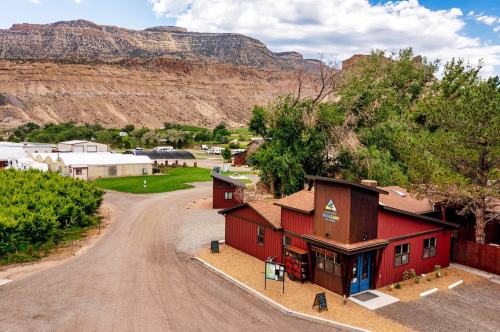A scenic view of a red building at the intersection of a gravel road, surrounded by green fields and mountains in the background.