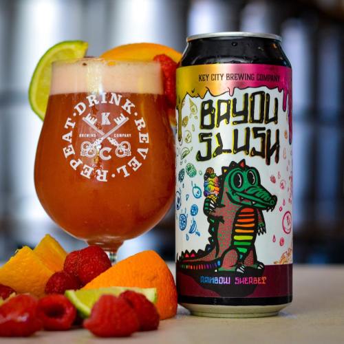 A colorful can of Bayou Slush beer next to a glass filled with a fruity drink, garnished with citrus and berries.