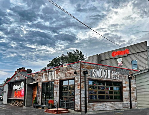 Exterior of Corry's BBQ restaurant with a rustic design, cloudy sky, and signage highlighting "Memphis Smokin' Since 1984."