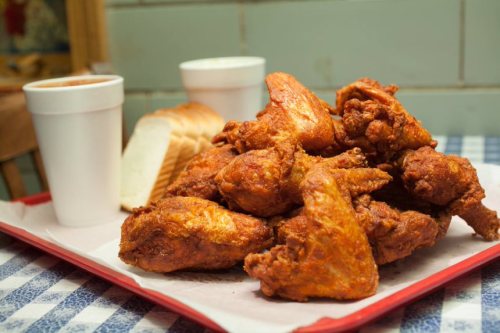 A platter of crispy fried chicken wings with two cups and slices of bread on a checkered tablecloth.