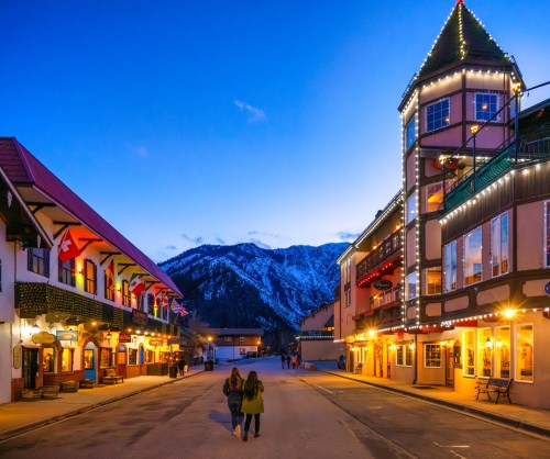 A charming street in a mountain town, lined with colorful buildings and twinkling lights at dusk.