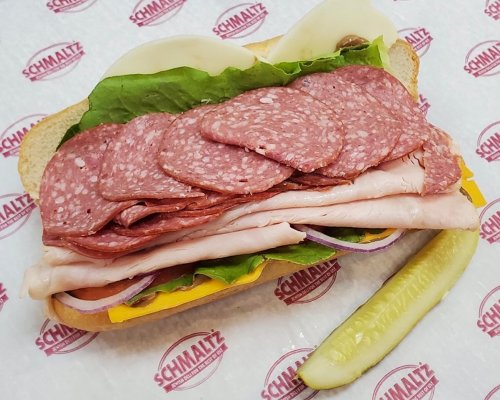 A hearty sandwich with layers of salami, turkey, lettuce, onions, and pickles on a toasted bun.
