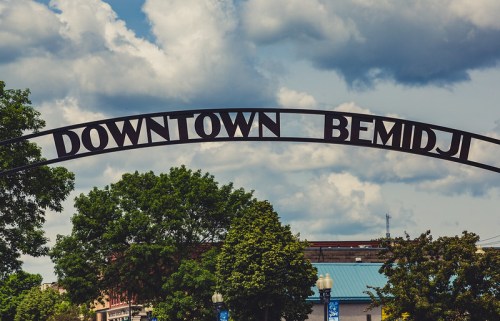Archway sign reading "Downtown Bemidji" with trees and a cloudy sky in the background.