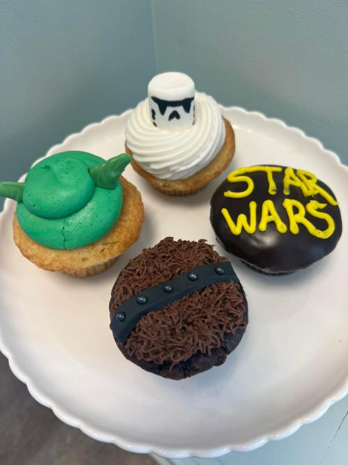 Four themed cupcakes: Yoda, a stormtrooper, a chocolate donut with Chewbacca design, and one with "Star Wars" written on it.