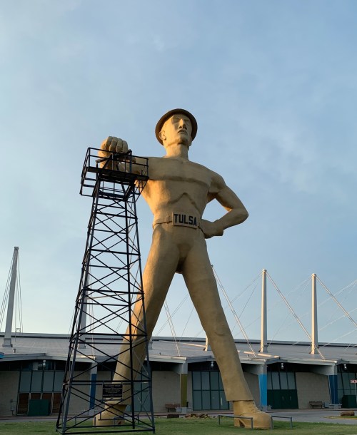 A large statue of a man in a hard hat stands next to a tower, with "TULSA" written on his waist.