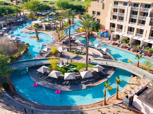 Aerial view of a resort pool area with palm trees, lounge chairs, and a winding lazy river.