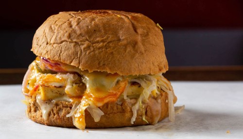 A close-up of a hearty burger with melted cheese, grilled chicken, and toppings on a toasted bun.