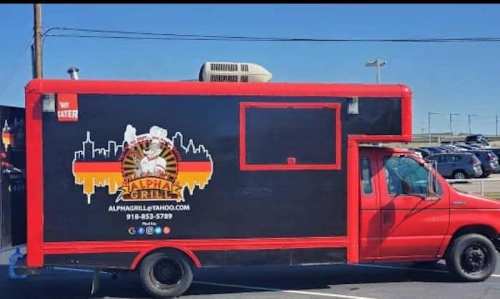 A red food truck with a black exterior featuring the logo "Alpha Grill" and a city skyline design.