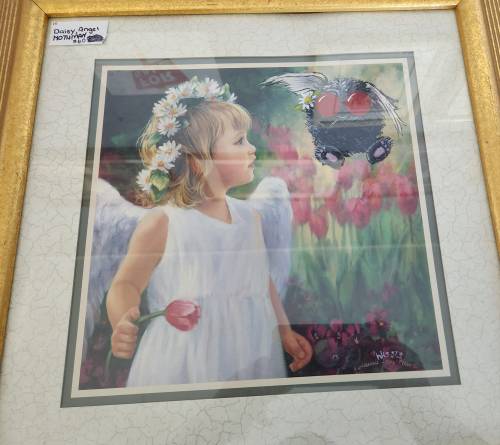 A framed artwork of a girl with angel wings holding a tulip, gazing at a whimsical creature with wings and red eyes.