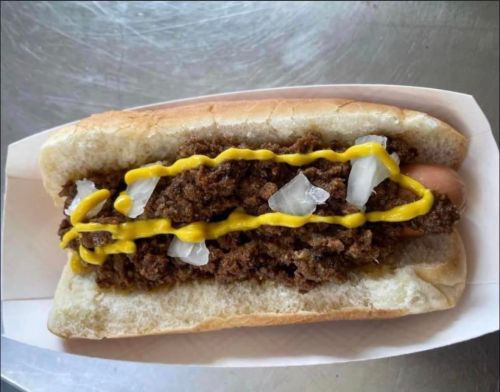 A hot dog topped with chopped onions and a generous layer of mustard, served in a soft bun.