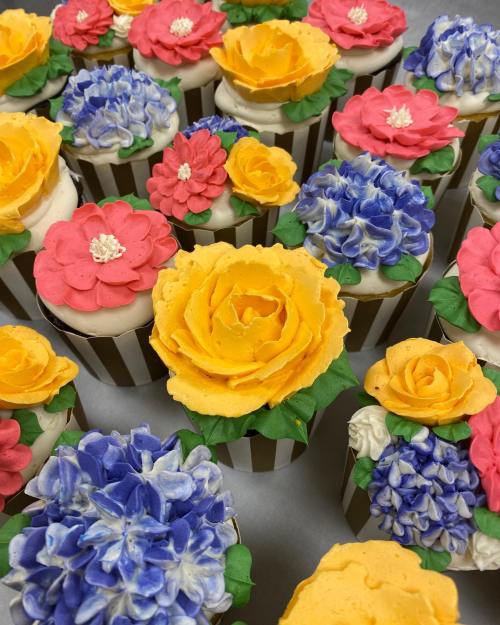 Colorful cupcakes decorated with vibrant flower designs in yellow, pink, and blue frosting.