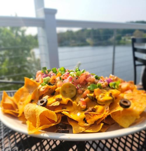 A plate of nachos topped with cheese, jalapeños, pico de gallo, and green onions, with a scenic view in the background.